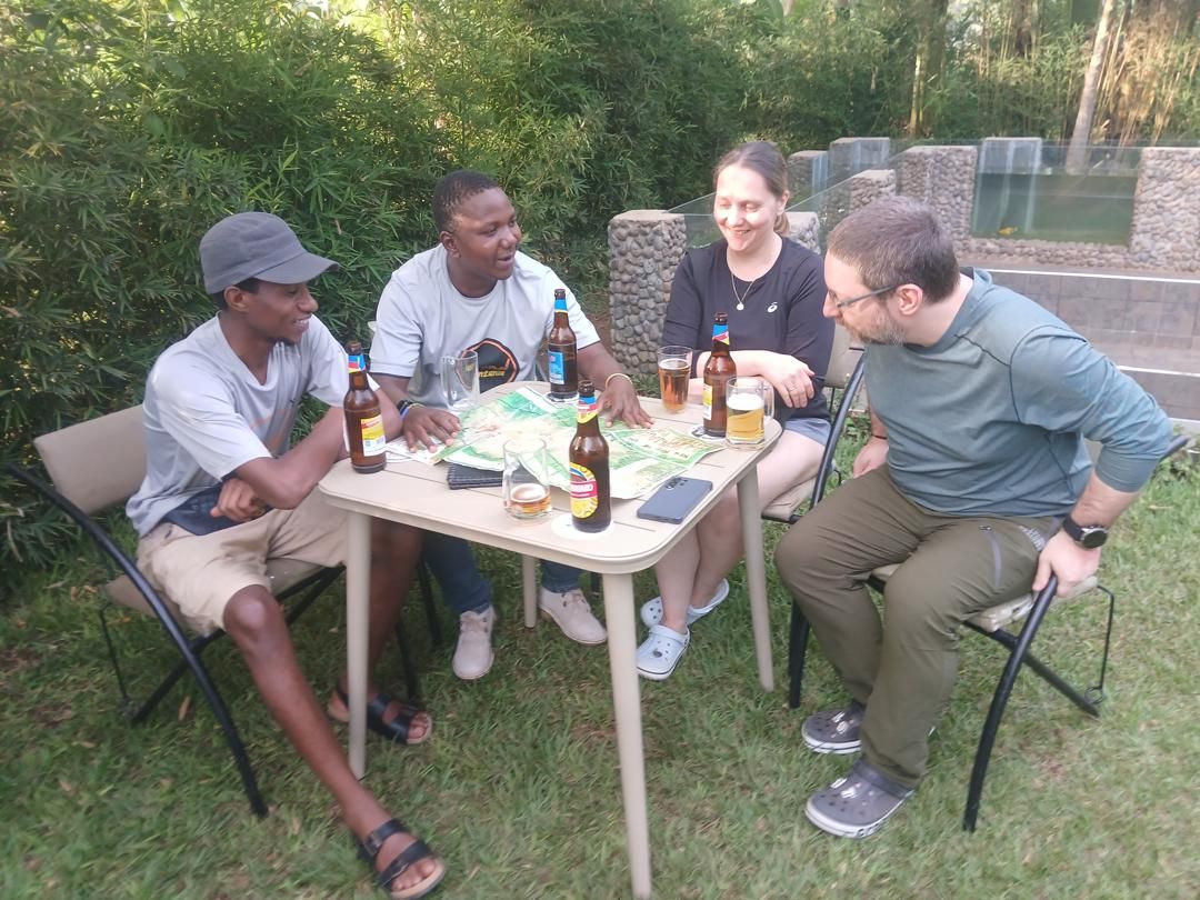 Two guides and two hikers talk over a large trail map and drinks at a garden table